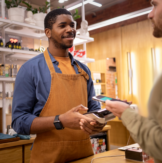Smiling cashier using a mobile payment terminal to process a contactless payment at a retail store.